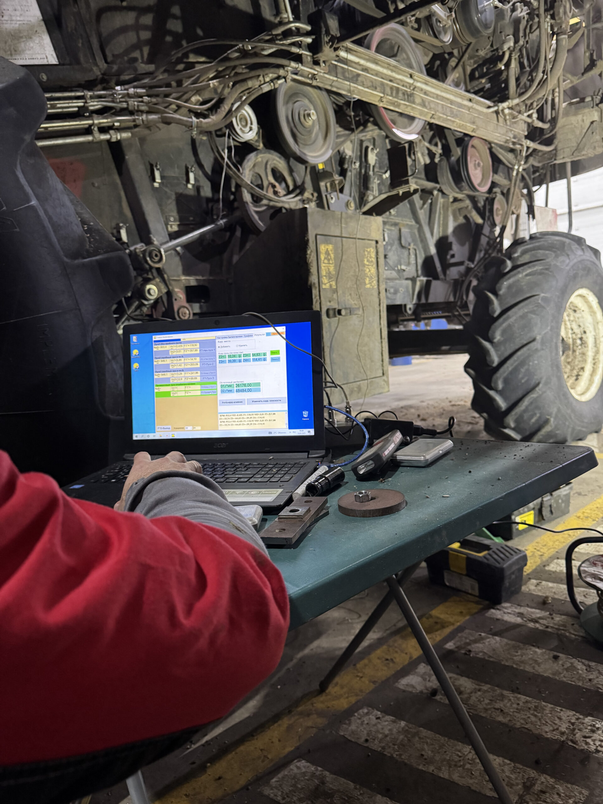 Field balancing of a combine harvester: specialist at a laptop running the Balanset software, correction weights and scales on the work table
