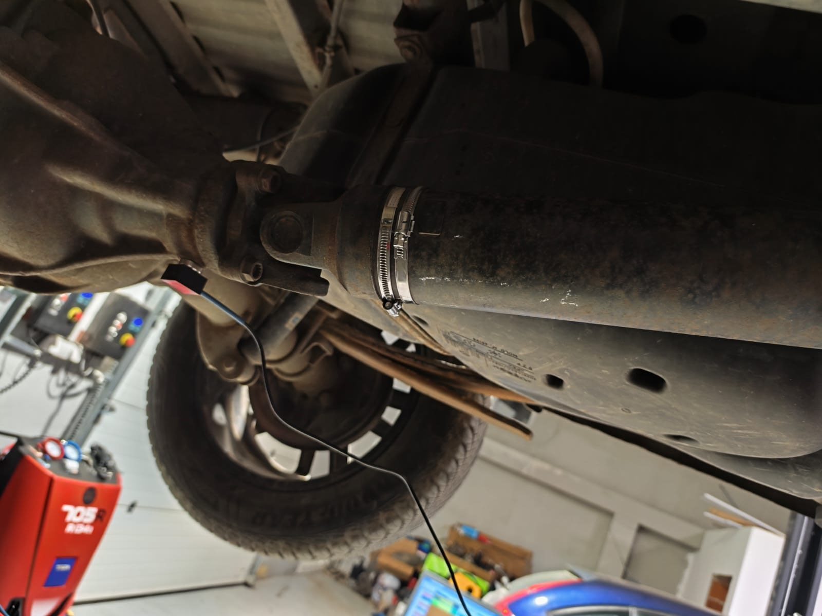 Correction weight secured to the driveshaft tube with a stainless hose clamp after in-vehicle balancing, with the vibration sensor cable running along the shaft