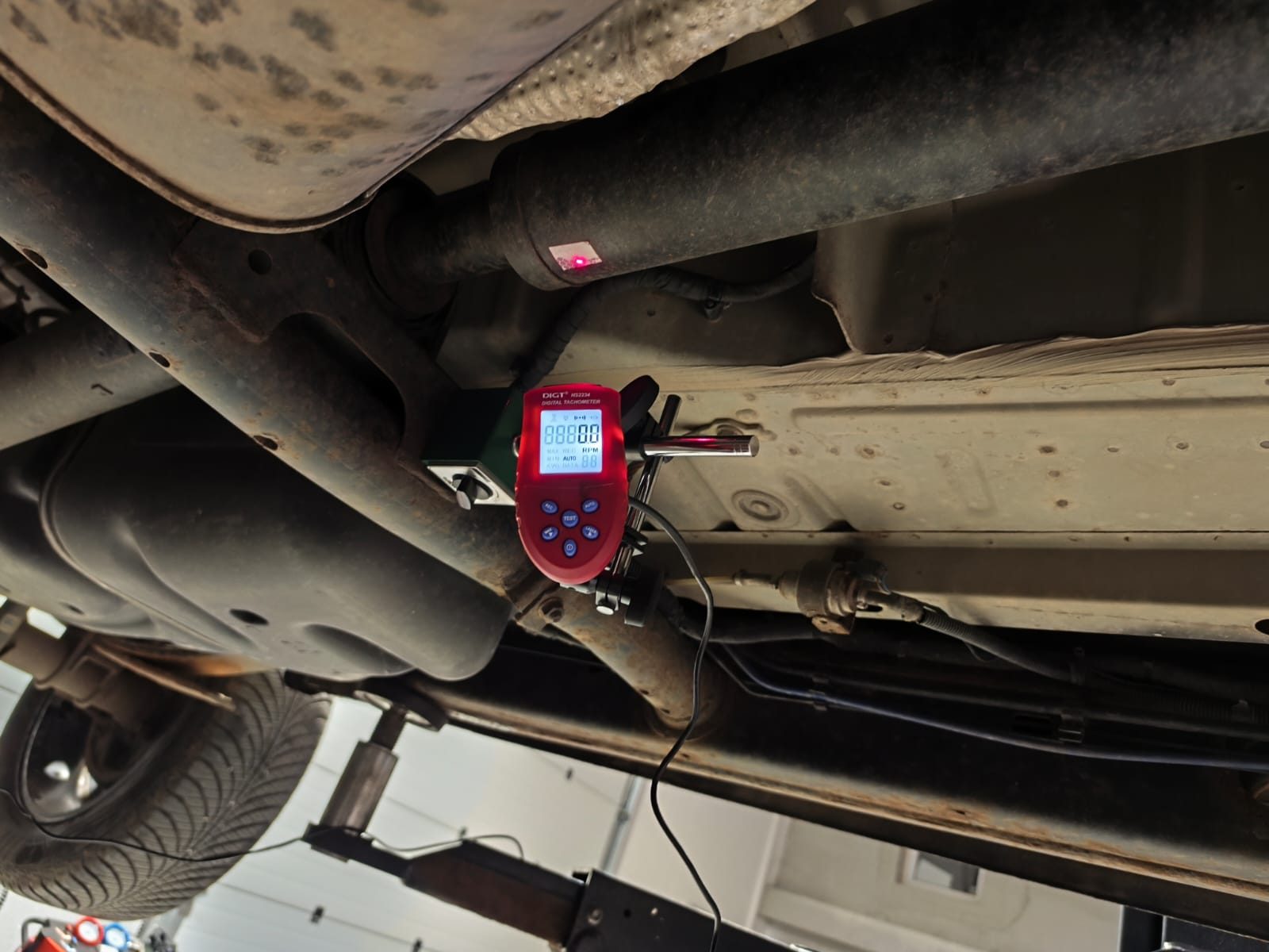 DIGT laser tachometer aimed at a reflective tape mark on the driveshaft to measure rotation speed and phase angle during in-vehicle balancing