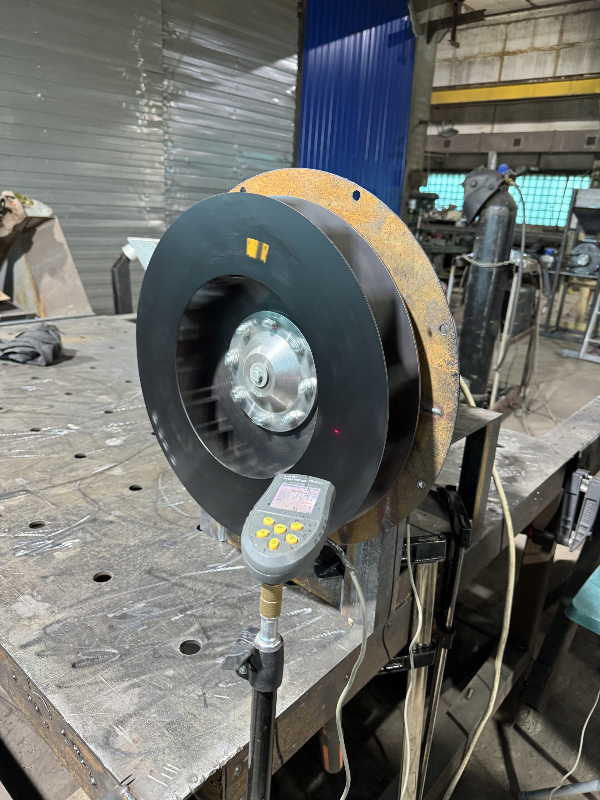 Fan impeller spinning on a workshop balancing stand, digital laser tachometer on a stand reading the reflective mark